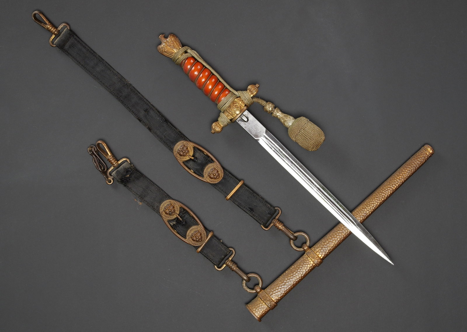 Dague de la Kriegsmarine. German Kriegsmarine dagger.: Dague de la Kriegsmarine. Garniture en metal, couleur or. Poignee en cellulod orange tirant sur le rouge. Dragonne complete et nouee de maniere reglementaire. Fourreau martele. Belieres completes, les