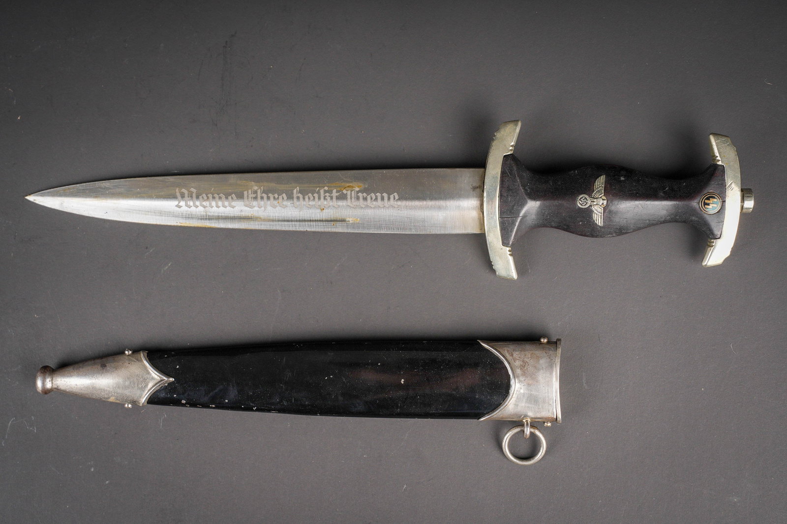 Dague SS. German SS Dagger: Dague SS. Modele 33. Garnitures en metal. Belle poignee en bois de couleur noire, quelques fissures visibles. Pastille SS et aigle allemand visiblement fixes d origine. Fourreau en metal, peinture noi