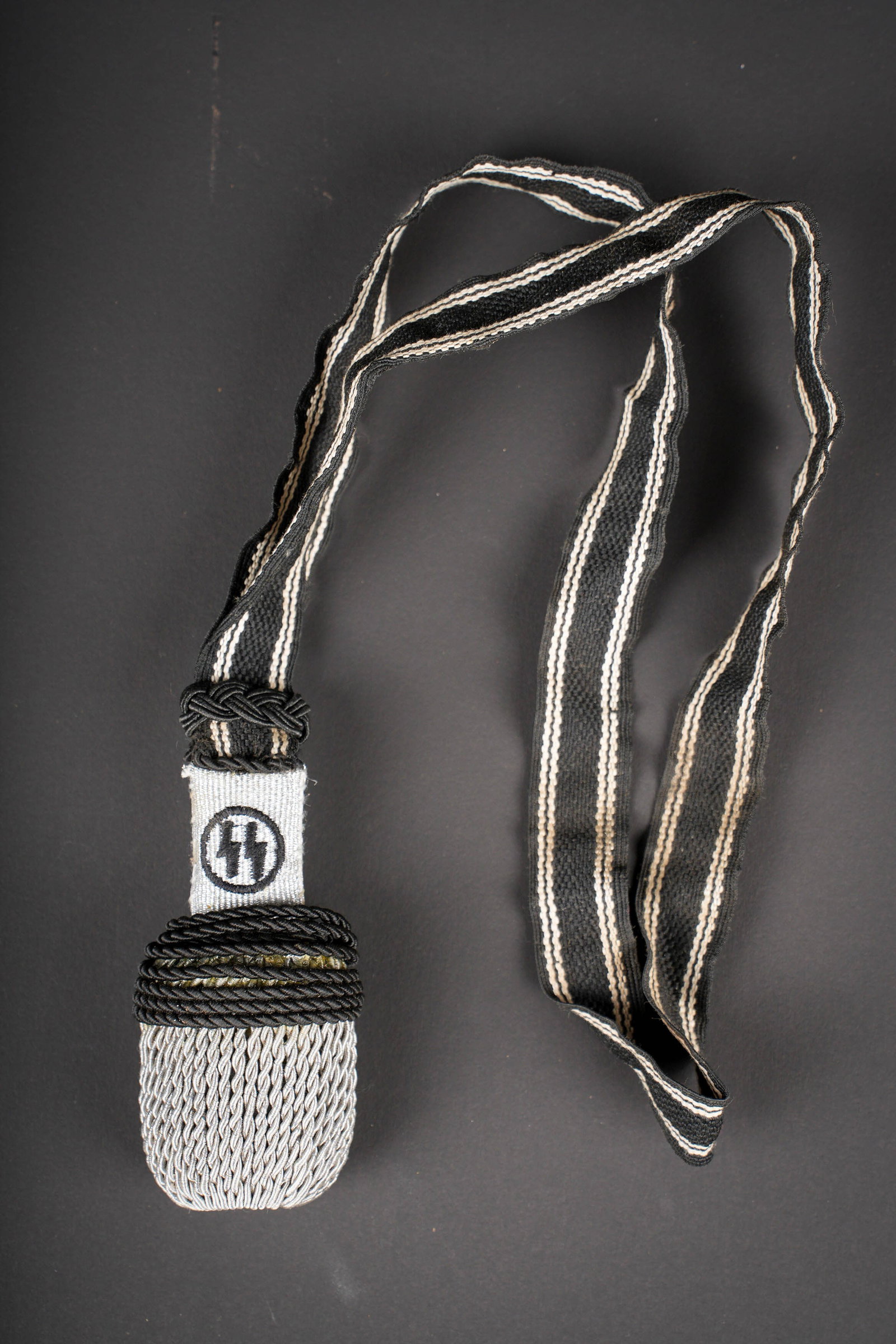 Dragonne SS. SS portepee.: Dragonne SS. Modele pour sous-officier. Passementerie en fil noir et argent. Base du gland en cannetille argent portant les deux runes SS, brodees de fils noir. Gland couleur argent et noir. A noter