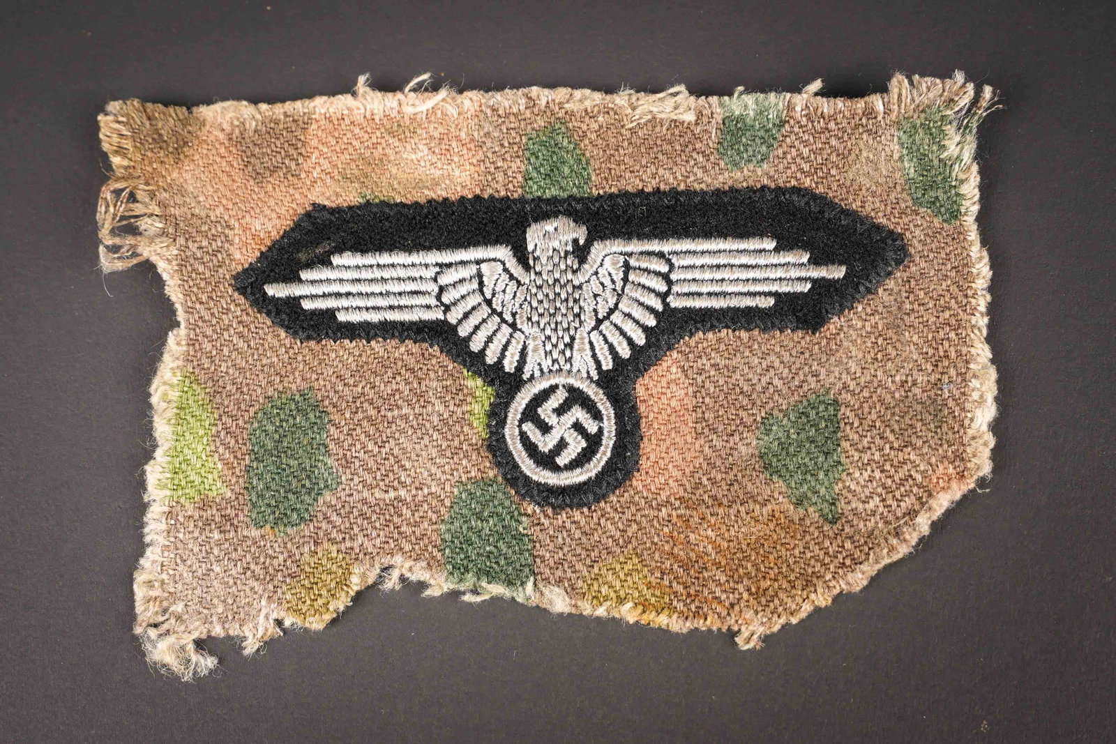 Aigle de bras SS decousu d une vareuse. SS sleeve eagle removed from a tunic.: Aigle de bras SS decousu d une vareuse petits pois. Modele brode sur fond noir cousu d origine sur un morceau de tissu camoufle petits pois. Insigne visiblement decoupe d une vareuse par un GI