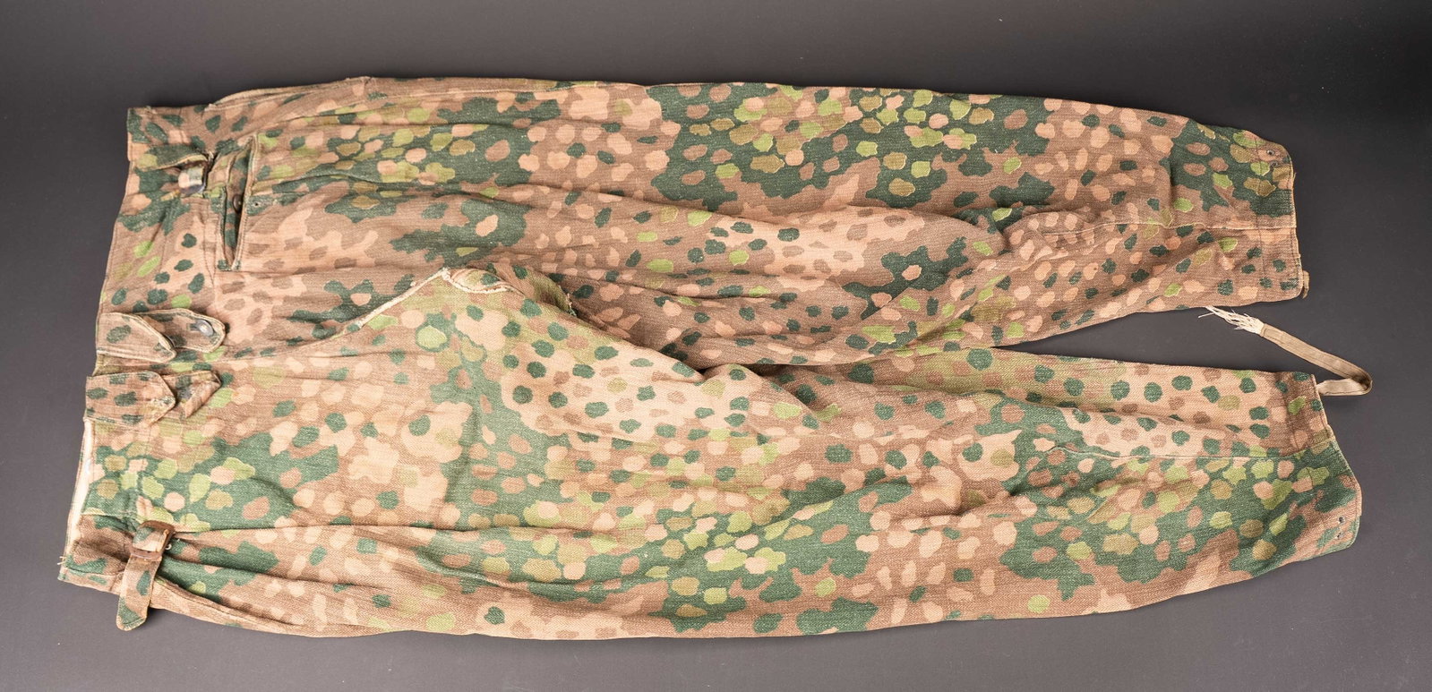 Pantalon petits pois SS. SS pea-dot camouflage trousers.: Pantalon petits pois SS. En tissu camoufle petits pois. Couleurs vives mais partiellement decolorees par le soleil. Tous les boutons sont presents, mais de modeles differents. Les lacets au bas des