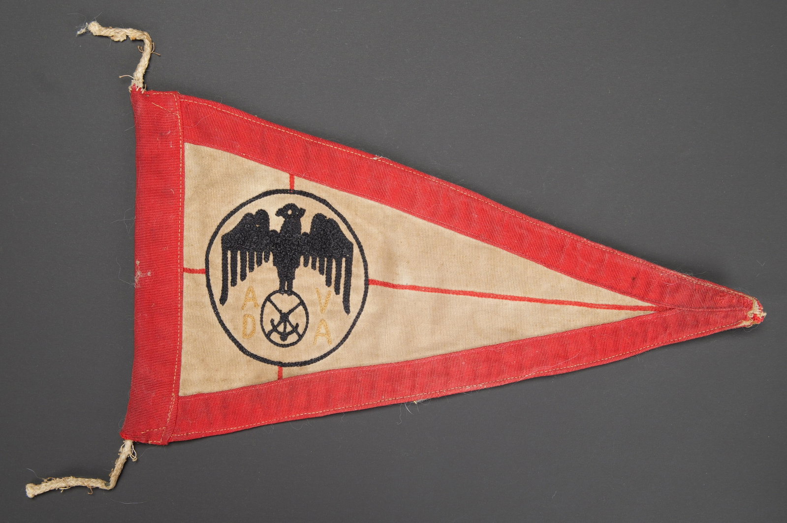 Fanion ADVA. German ADVA pennant.: Fanion ADVA. Modele triangulaire en tissu coton rouge et blanc. Aigle brode, ainsi que le lettrage ADVA. Dimensions 16,5 x 28,5 cm. Les cordelettes sont incompletes. A noter une certaine usure et