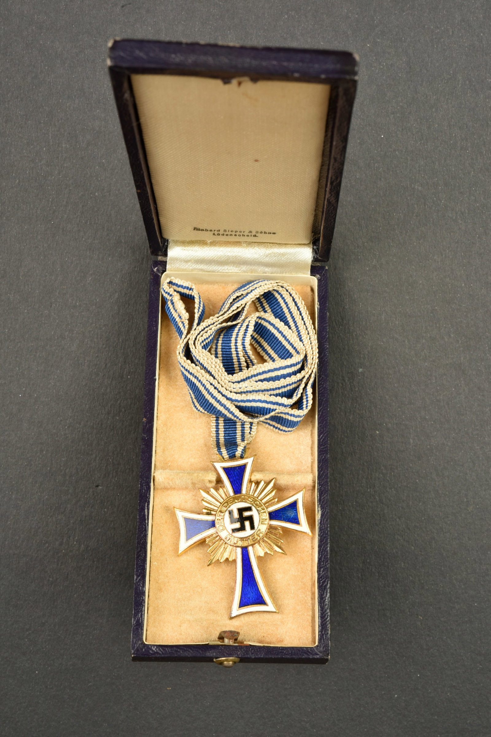 Mutterkreuz. Mother?s Cross: Mutterkreuz. Belle boite de couleur bleu fonce. Mutterkreuz estampillee sur le couvercle. Fermoir complet. Interieur double en velours et satinette blanche. Fabrication Robert Sieper Ludenscheid.