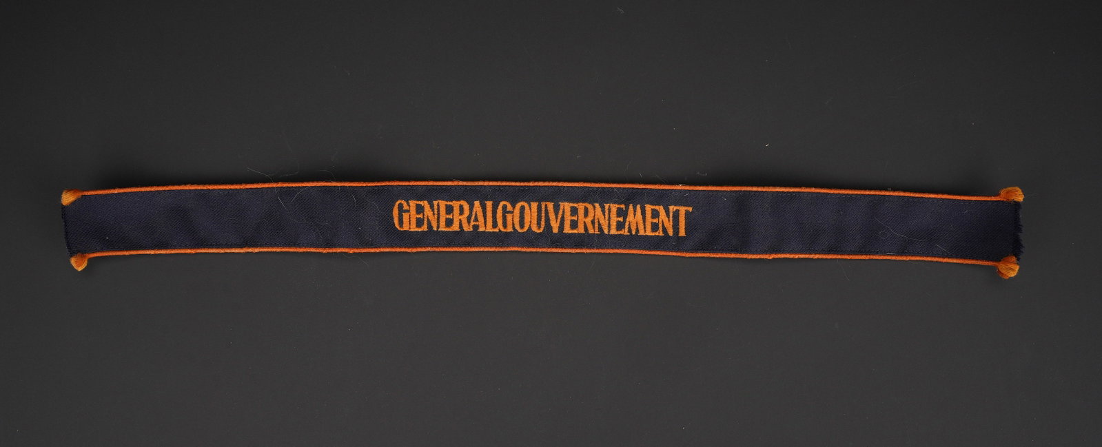 Bande de bras GeneralGouvernement. General Government armband.: Bande de bras GeneralGouvernement. En tissu bleu marine. Double lisere orange. Broderie Generalgouvernement egalement de couleur orange. Longueur 49 cm. Hauteur 3,7 cm. A noter une certaine usure et