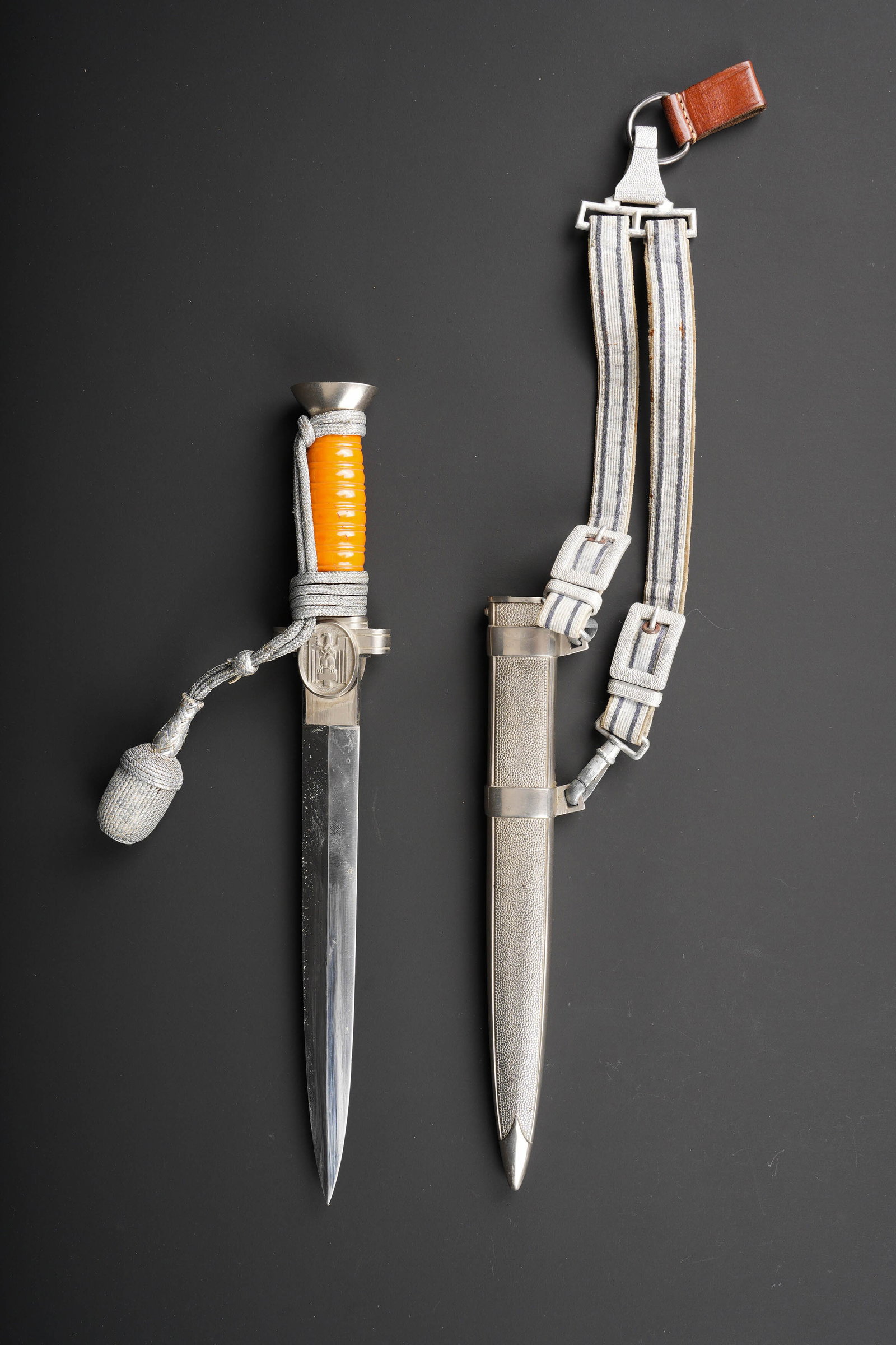 Dague DRK. German Red Cross Dagger.: Dague DRK. Garnitures en metal. Poignee en cellulod jaune. Belle lame presentant quelques traces d oxydation. Sans marquages fabricant visibles. Dragonne couleur argent, nouee de maniere