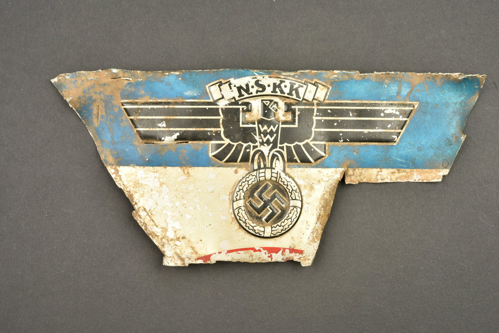 Insigne NSKK. German NSKK insignia: Insigne NSKK. Bel insigne en tole embouti type aluminium, provenant certainement d un vehicule. Reste de peinture bleue et rouge. A noter une certaine usure et patine de la piece. Dimensions 14 x 31 c