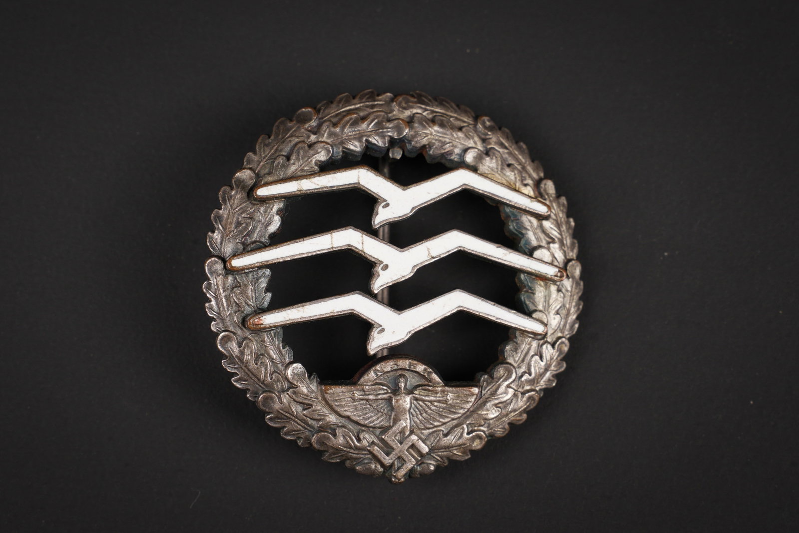 Insigne de pilote de planeur NSFK. NSFK glider pilot badge.: Insigne de pilote de planeur NSFK. En metal, couleur argent a 70%. Trois mouettes en metal emaille blanc, quelques craquelures presentes. Attache complete. Dos de la piece oxydee. Les marquages sont