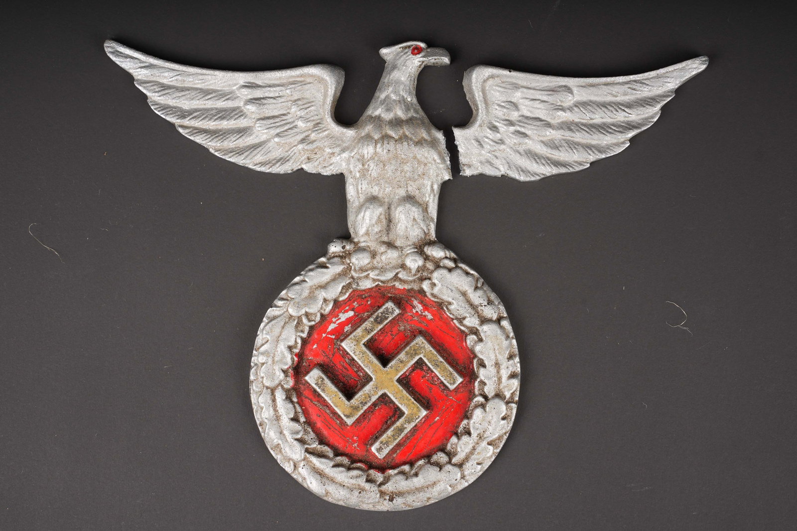 Aigle murale allemand. German wall eagle.: Aigle mural allemand. En metal. Une aile cassee et recollee. Insigne national en relief, fond rouge visiblement repeint. ?il de l aigle egalement en couleur rouge. Sans marquages visibles. Dimensions