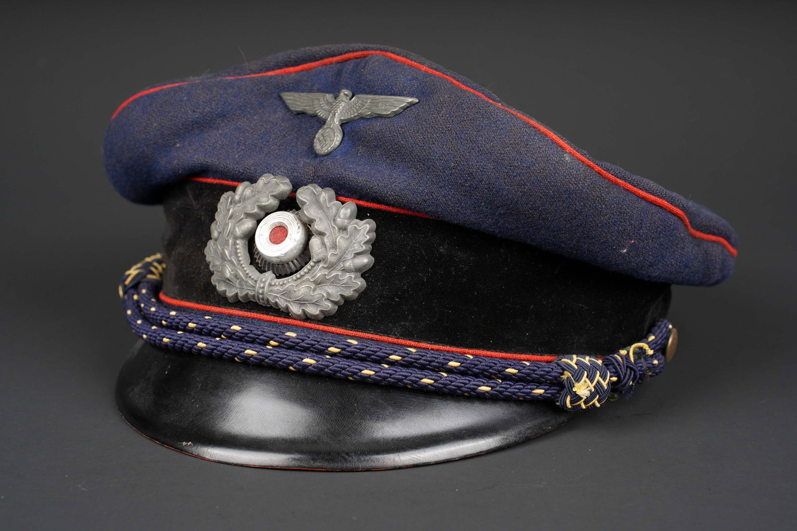 Casquette de la Reichsbahn. Deutsche Reichsbahn visor cap.: Casquette de la Reichsbahn. En drap bleu marine. Lisere rouge. Bandeau en velours noir. Insignes metalliques. Les insignes n ont pas ete demontes afin de verifier les attaches. Jugulaire complete,