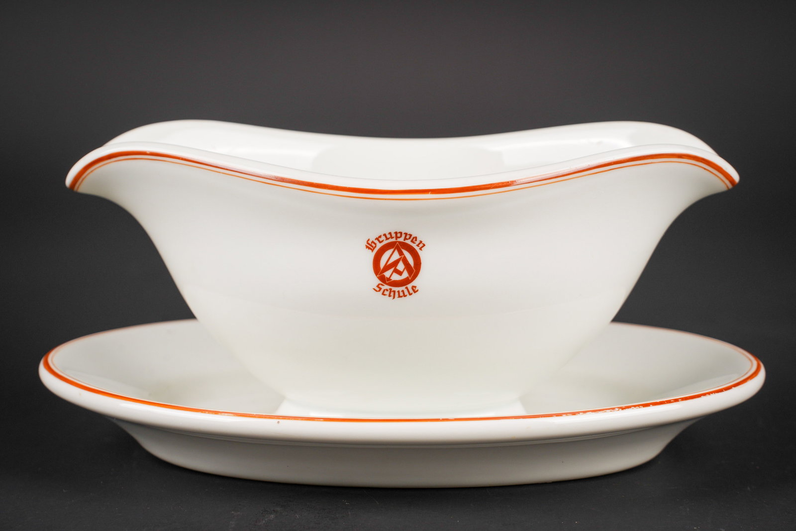 Sauciere SA. SA gravy boat.: Sauciere SA. En ceramique blanche. Liseres rouge. Marquage au niveau de la face avant Gruppen SA Schule. Fabrication Bohemia. Longueur environ 27 cm. L authenticite de la piece n est pas garantie. A