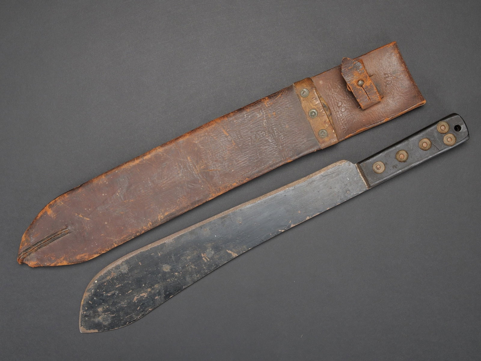 Machette britannique. British machete.: Machette britannique. Plaquettes de couleurs noires, maintenues pas cinq rivets. Belle lame de couleur noire. Les marquages sont presents, mais illisibles. Fourreau en cuir marron. La sangle de fermet