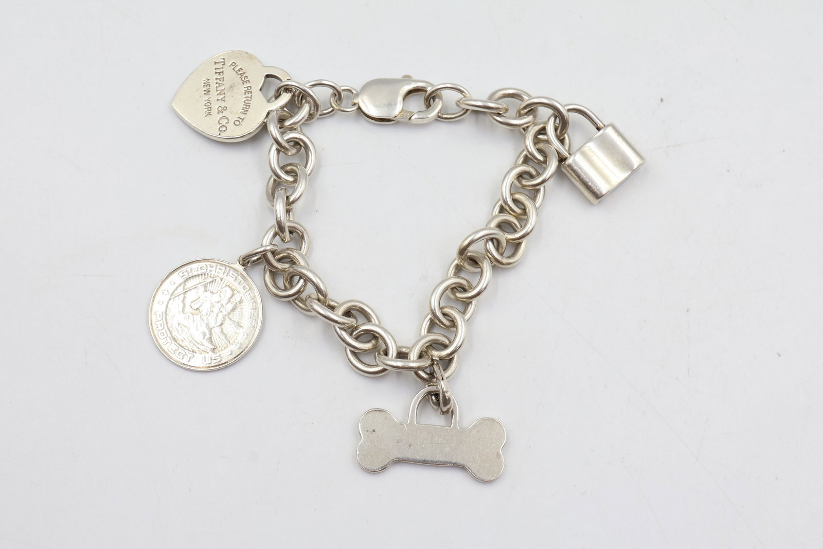 Tiffany & Co Charm Bracelet w/ 4 charms: Tiffany and Co charm bracelet has 4 charms. A heart, bone, lock and st christophers charms all stamped Tiffany & Co and 925. Comes with pouch. Total weight is 51 g. Fits a 7" wrist.