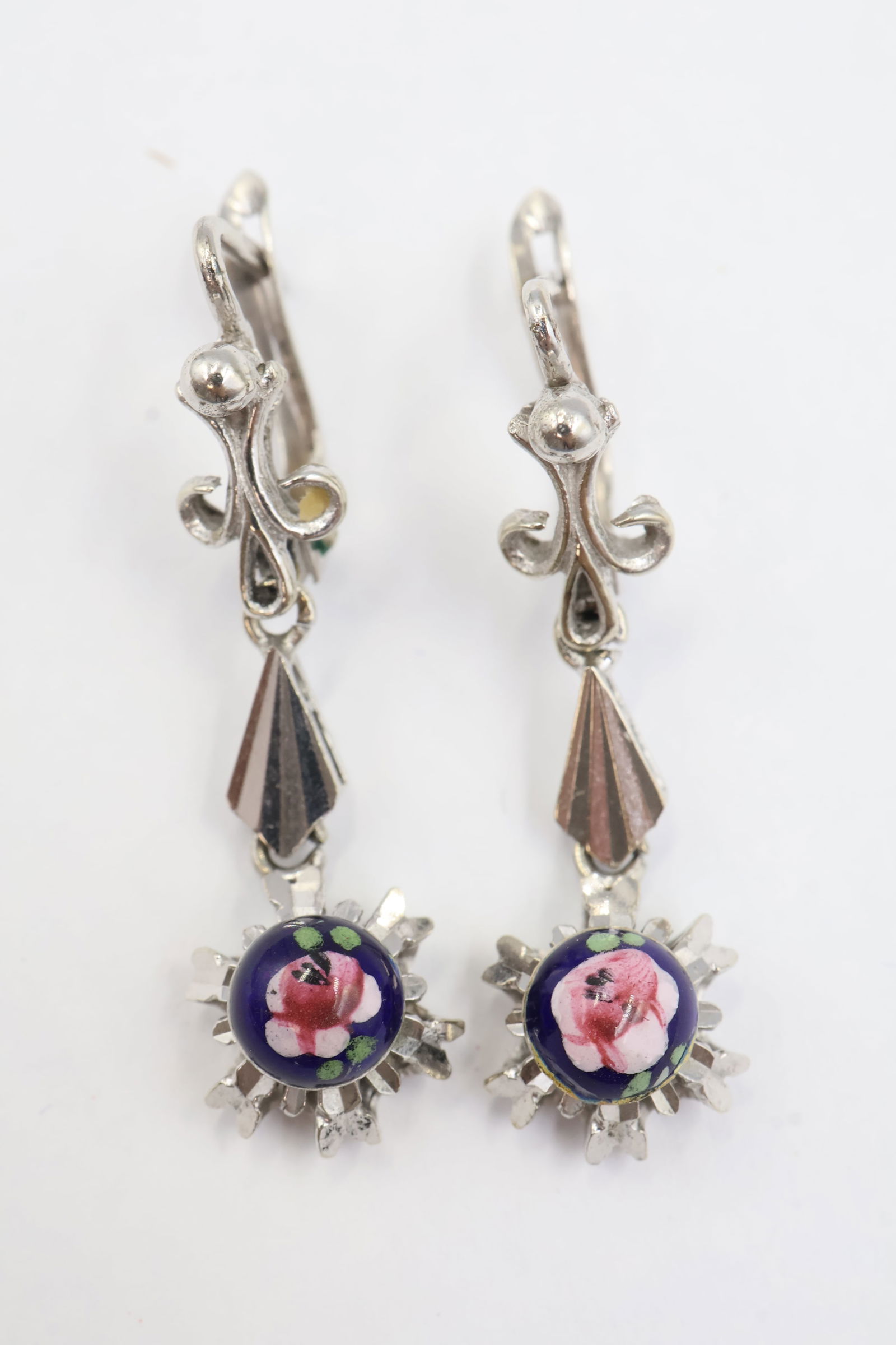 18K White Gold Hand Painted Pink Flower Blue Enamel Dangle Earrings: Elegant and eye catching, these dangle earrings feature a delicate hand painted pink flower set against rich blue enamel. Crafted in solid 18K white gold and weighing 6.1 grams, they offer a luxurious