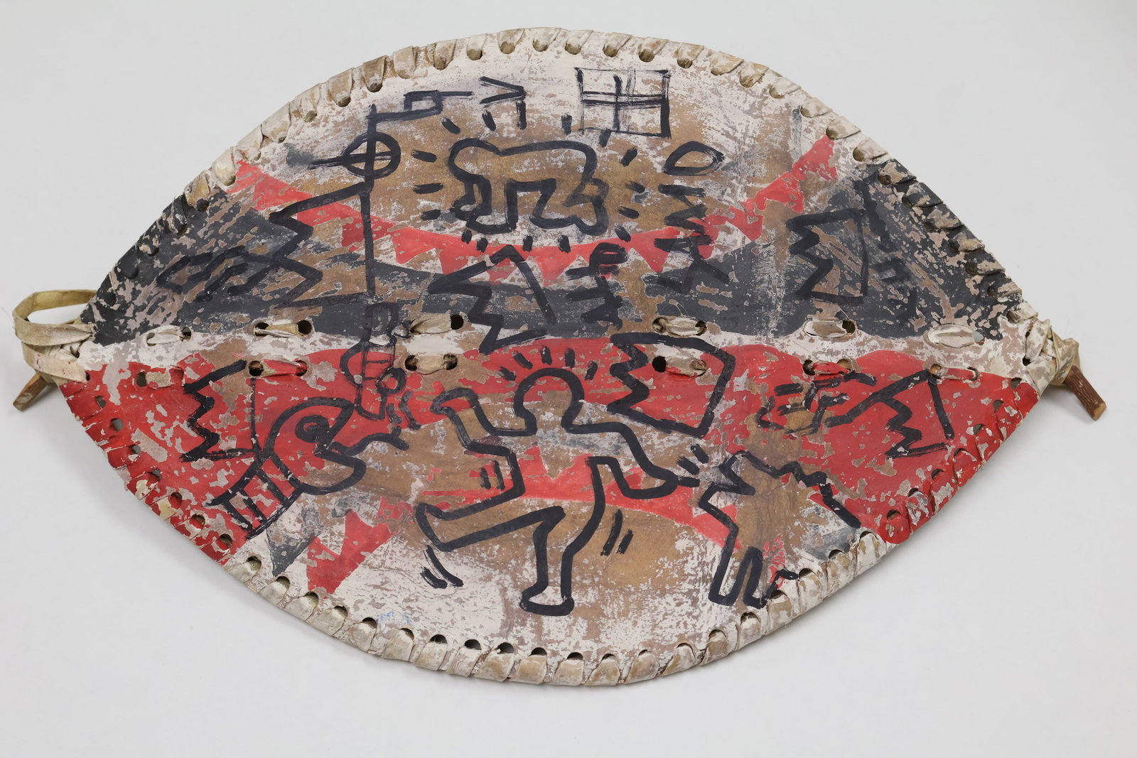 Haring-Basquiat: Felt tip black marker over red, black anid white paint on a African leather shield. This very rare example comes with lengthy provenance including CoA signed by Patti Astorr. Dimensions: 16 x 10 inche