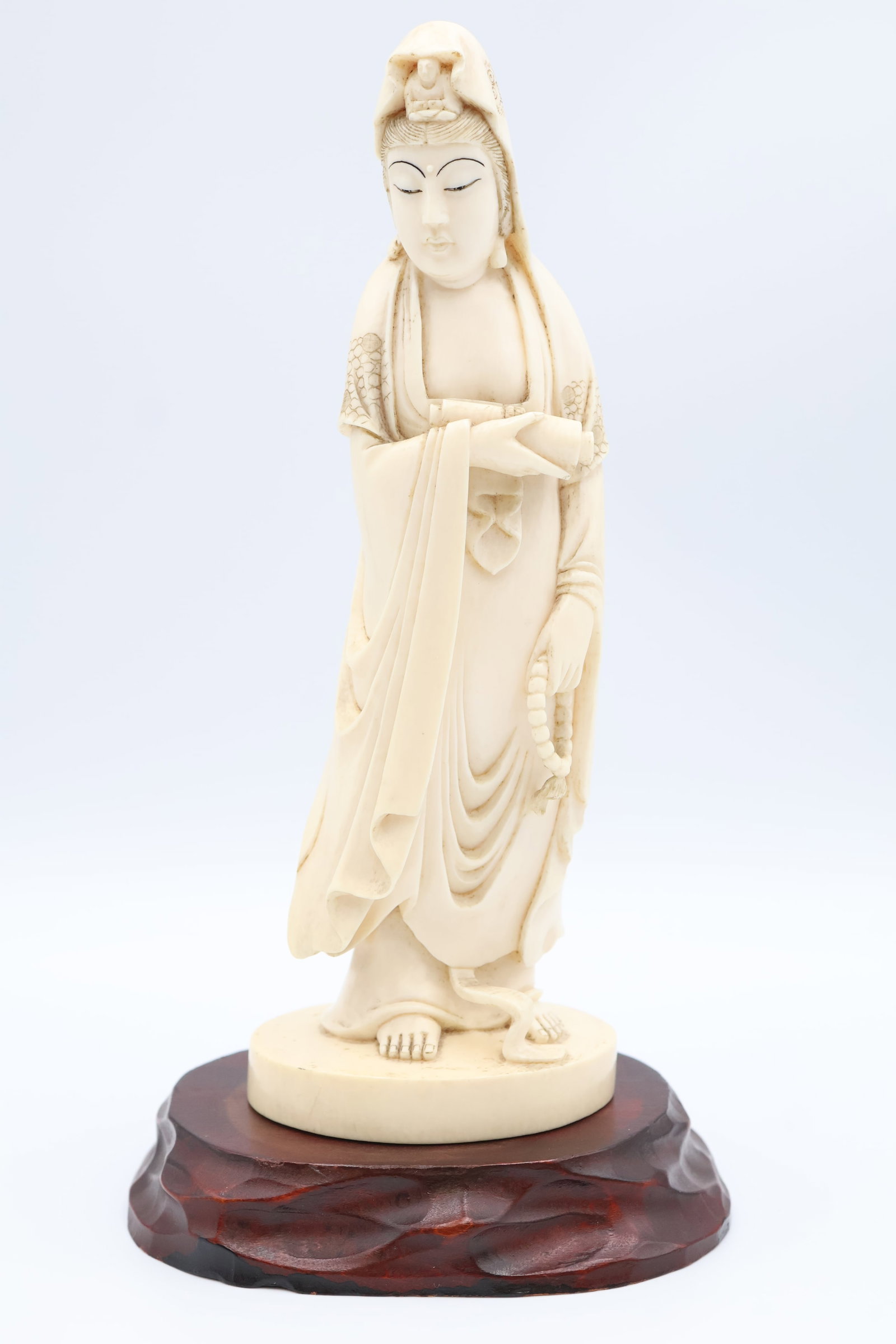 Hand Carved ChineseFigural Study: The finely detailed standing Guanyin (Bodhisattva of Compassion) is adorned withdraped robes bearing a serene expression. The figure supports a string of prayer beads and a jar or scroll in the other