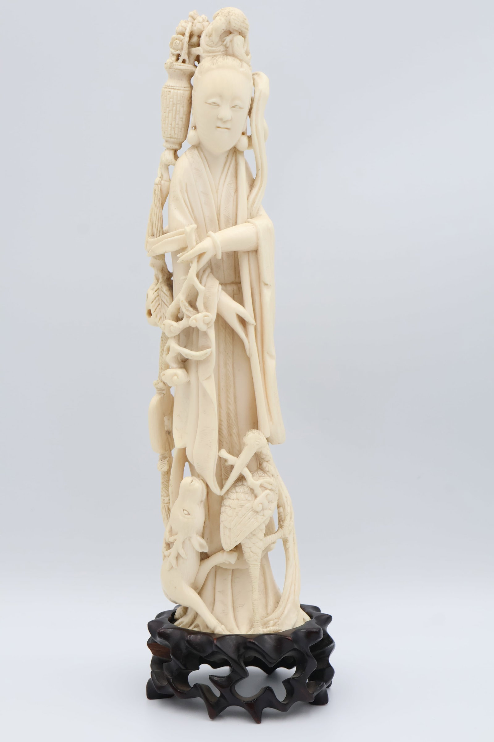 A Hand Carved Japanese Okimono of “Guanyin”: The reticulated carving shows a standing deity holding a blossoming branch with animals at her feet. Goddess of Mercy, dimensions: 10” height (not including hand carved reticulated wood stand).