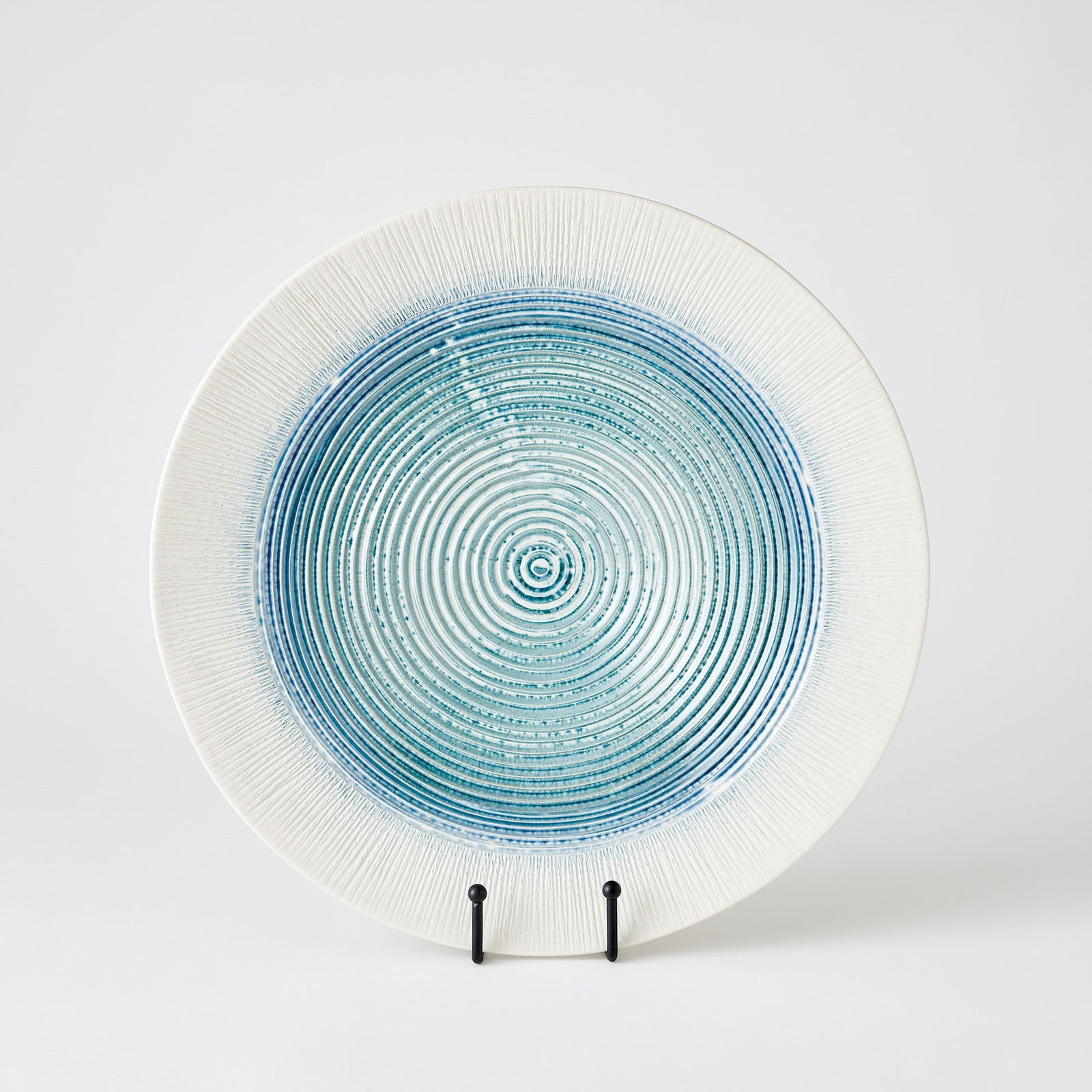 Ribbed Charger In Lambs Ear: Ribbed Charger In Lambs Ear Crafted by Portuguese artisans, the Ribbed Charger is made of slip-molded ceramic with a lamb's ear and white finish. Each radial line is hand-painted with a reactive glaze