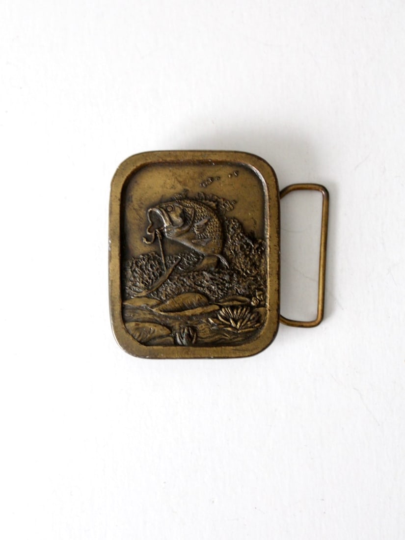 Vintage 70S Brass Bass Fishing Buckle: Vintage 70S Brass Bass Fishing Buckle This is a 1970s vintage brass buckle. The tall rectangle buckles pictures a bass fish jumping out of the water. Great raised design. Post and loop back. CONDITION