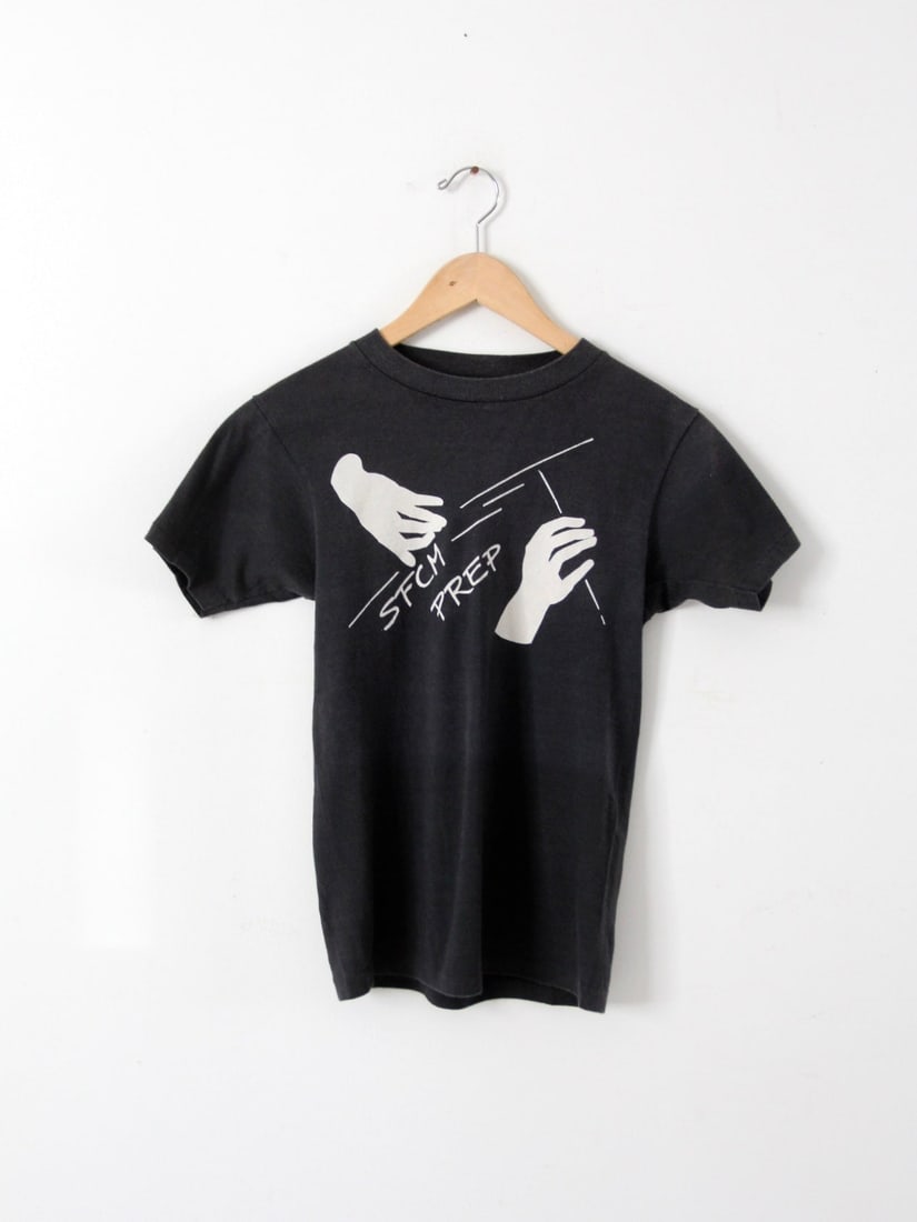 1980s Vintage SFCM Graphic Tee Black Crew Neck T-Shirt: 1980s Vintage SFCM Graphic Tee Black Crew Neck T-Shirt Embrace a piece of musical history with this vintage 1980s SFCM graphic tee. Crafted from soft, faded fabric, this black crew neck t-shirt showca