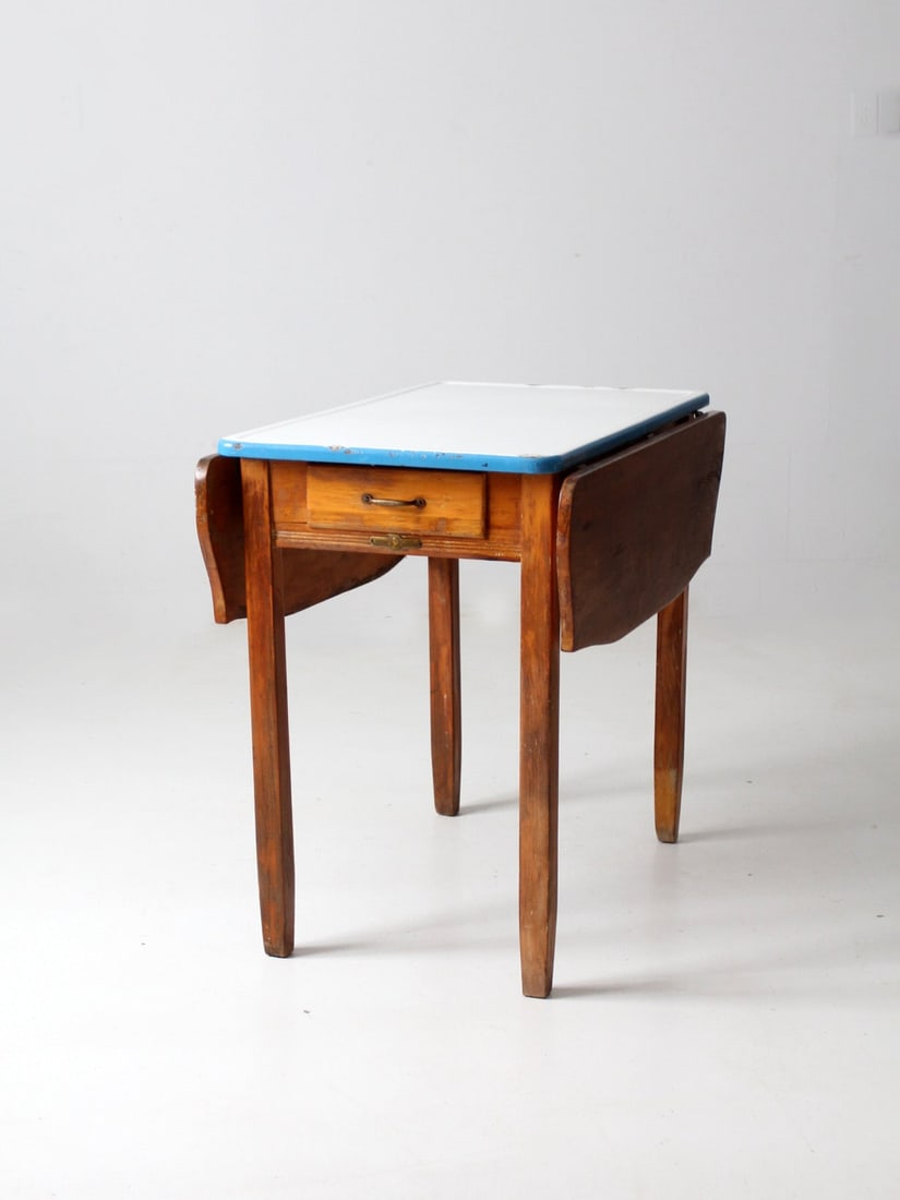 Vintage Napanee Drop Leaf Kitchenette Table with Enamel Top: Vintage Napanee Drop Leaf Kitchenette Table with Enamel Top This charming kitchenette table, crafted by Napanee Coopes Brothers & Zook between 1913 and 1935, features a classic design with a white ena