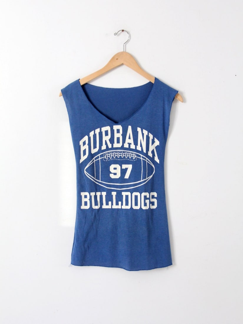 1980s Vintage Burbank Bulldogs Fitted Tank Top: 1980s Vintage Burbank Bulldogs Fitted Tank Top Step back into the 1980s with this vintage Burbank Bulldogs tank top. This fitted tank is re-cut from a classic blue graphic tee and features a stylish v