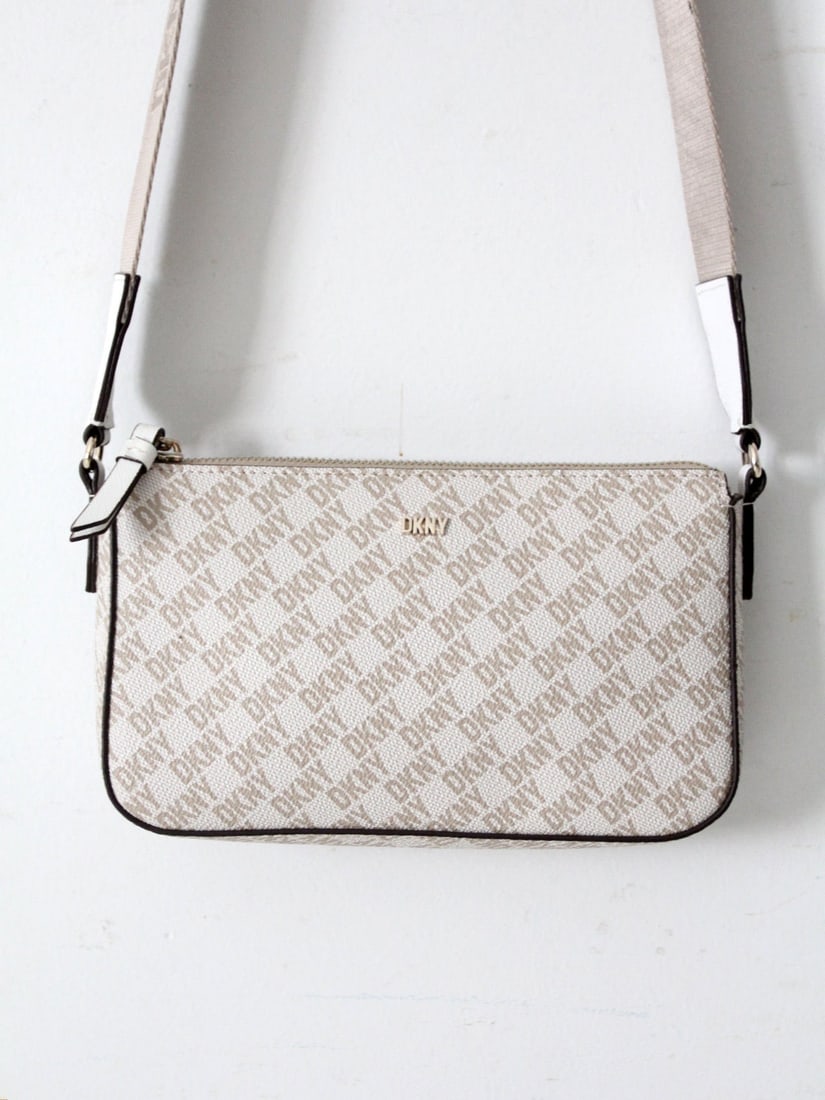 DKNY Bryant Demi Crossbody Bag with Monogram and Gold Tone Hardware: DKNY Bryant Demi Crossbody Bag with Monogram and Gold Tone Hardware The DKNY Bryant Demi Crossbody Bag showcases a perfect blend of timeless minimalism and modern logo aesthetics. This compact handbag