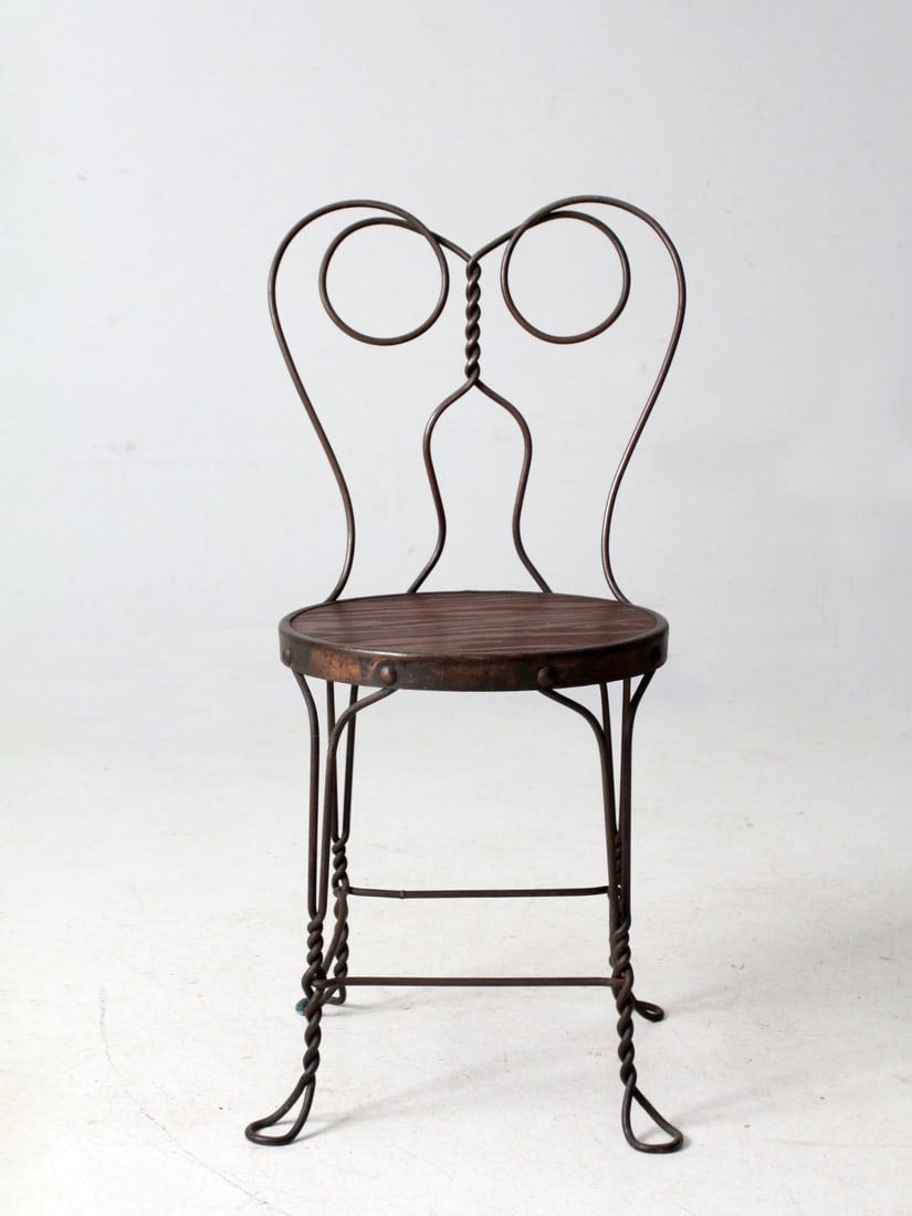 Vintage Wrought Iron Ice Cream Parlor Chair with Wooden Seat: Vintage Wrought Iron Ice Cream Parlor Chair with Wooden Seat This antique wrought-iron bistro chair features a graceful scroll back and a round wooden seat, showcasing a sculptural design ideal for