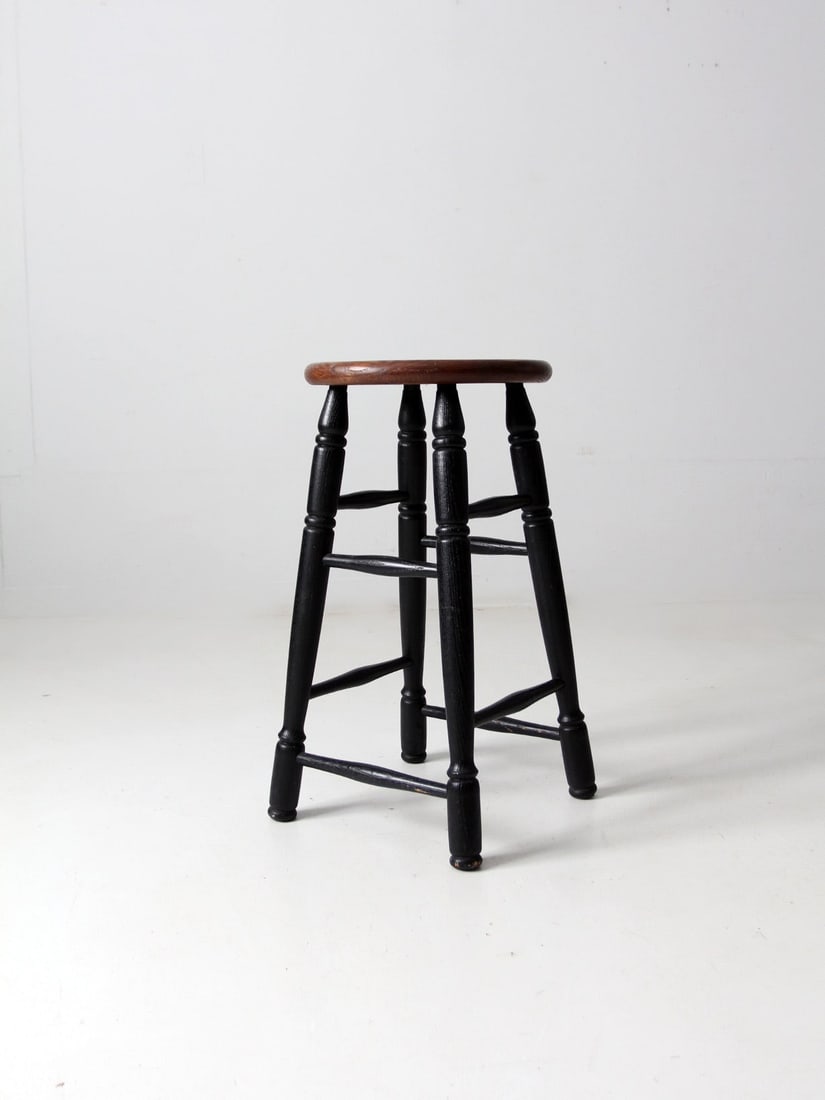 Classic Vintage Wooden Stool with Black Turned Legs: Classic Vintage Wooden Stool with Black Turned Legs This vintage wooden stool showcases a classic design with black turned legs and a round wooden seat. Its sturdy construction ensures durability,