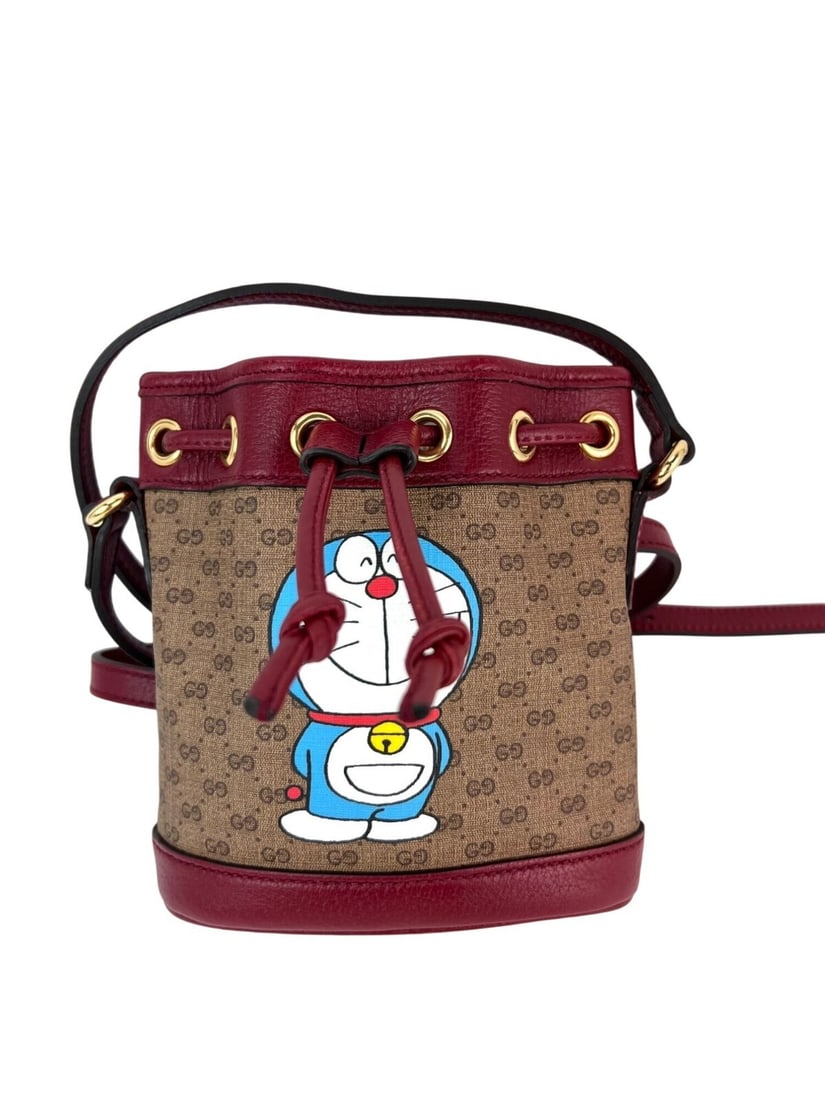 Gucci X Doraemon Vintage GG Supreme Mini Bucket Bag Red Strap: Gucci X Doraemon Vintage GG Supreme Mini Bucket Bag Red Strap Elevate your accessory game with the Gucci X Doraemon Vintage GG Supreme Mini Bucket Bag. This stylish round bag features a classic GG mon