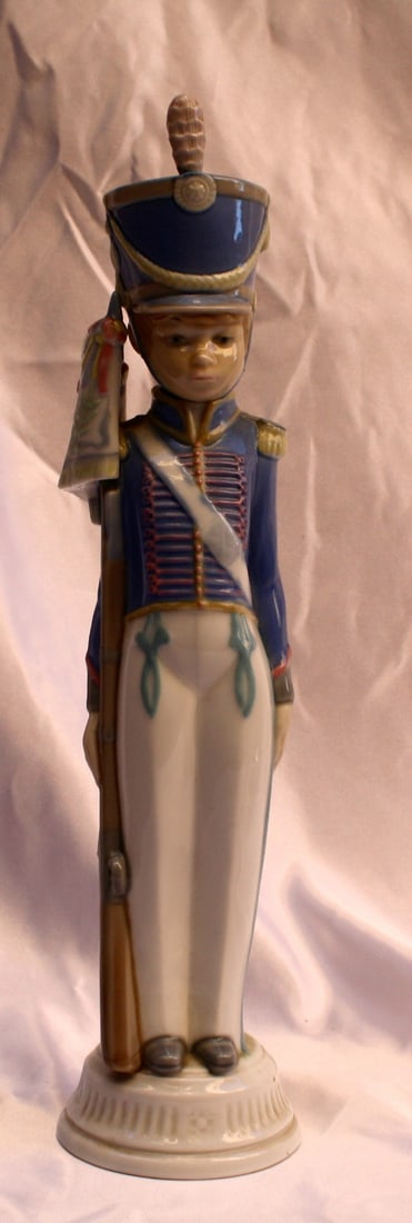 Lladro Hand-Painted Porcelain Soldier Figurine with Flag and Box: Lladro Hand-Painted Porcelain Soldier Figurine with Flag and Box This exquisite Lladro figurine features a hand-painted soldier proudly holding a flag and a gun. Crafted from fine porcelain, it stands
