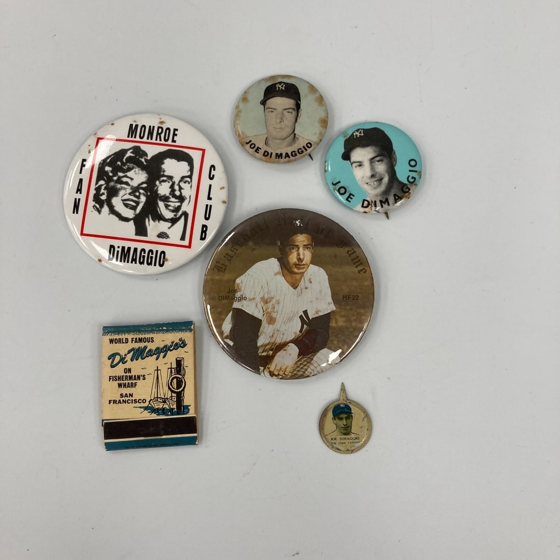 5 Vintage Joe DiMaggio Pins with Dimaggio Restaurant Matchbook: 5 Vintage Joe DiMaggio Pins with Dimaggio Restaurant Matchbook This collection features five vintage pins from the 1938 and 1940s era, celebrating the legendary Joe DiMaggio, along with a matchbook fr