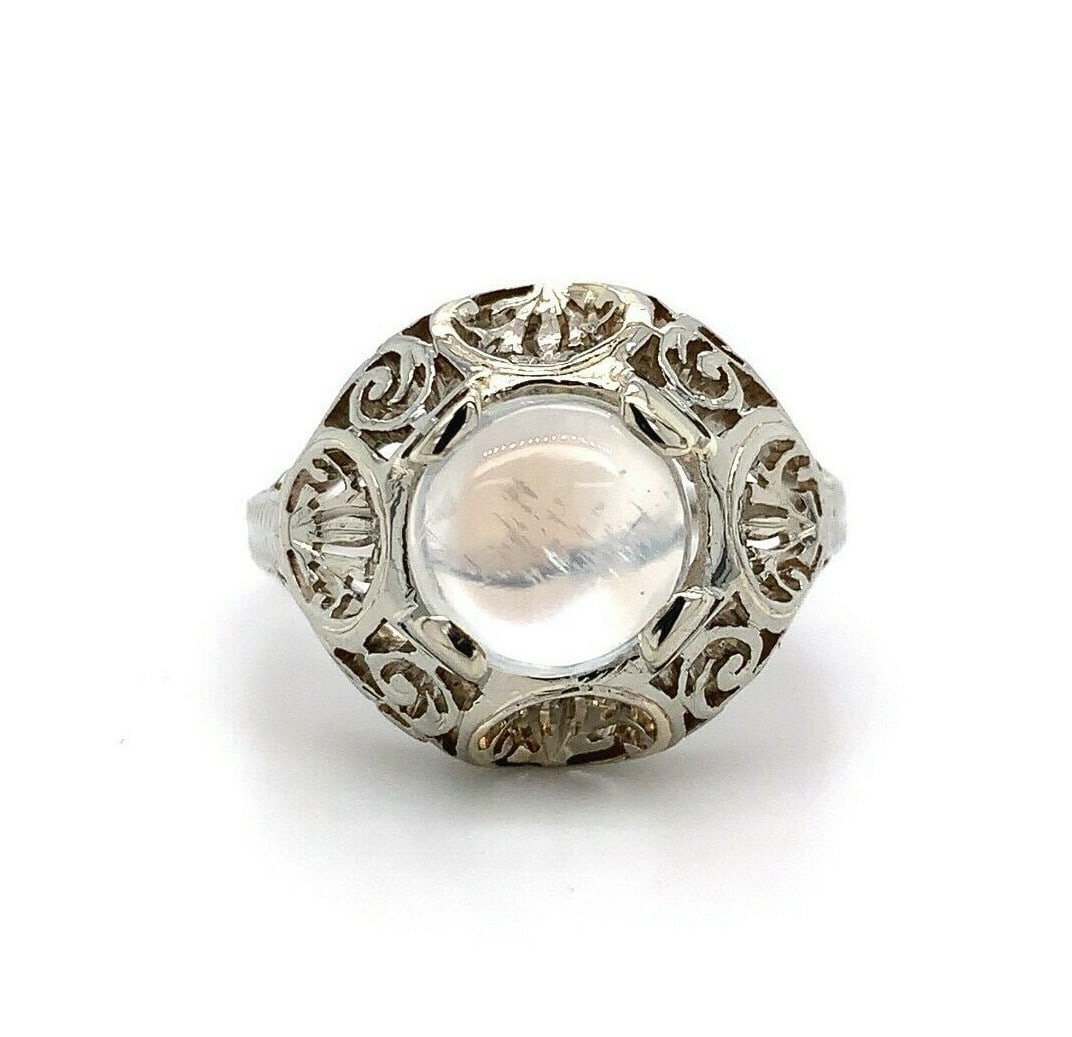 Art Deco 18k White Gold Filigree Moonstone Ring 1.66ct Blue Flash: Art Deco 18k White Gold Filigree Moonstone Ring 1.66ct Blue Flash This exquisite 18k white gold ring showcases a stunning round moonstone with a captivating blue flash. The unique hand-pierced filigre