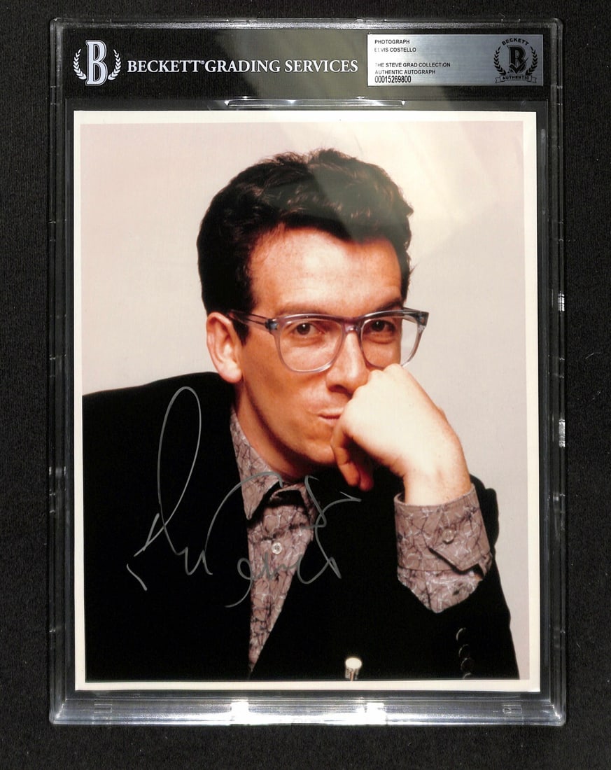 Elvis Costello Signed 8x10 Photograph Beckett Authenticated: Elvis Costello Signed 8x10 Photograph Beckett Authenticated This remarkable 8x10 photograph features the legendary Elvis Costello, who has signed it in silver permanent marker. The autograph, authenti