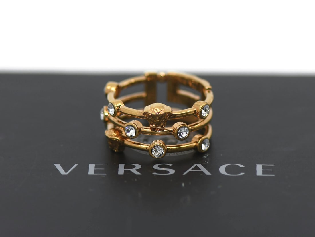Gold Plated Versace Ring in 8.5 Size: Gold Plated Versace Ring in 8.5 Size This is a Versace gold plated ring in a size 8.5, featuring a width of 12mm and a weight of 5.4 grams. The ring is pre-owned and offers a bold, designer style. Spe