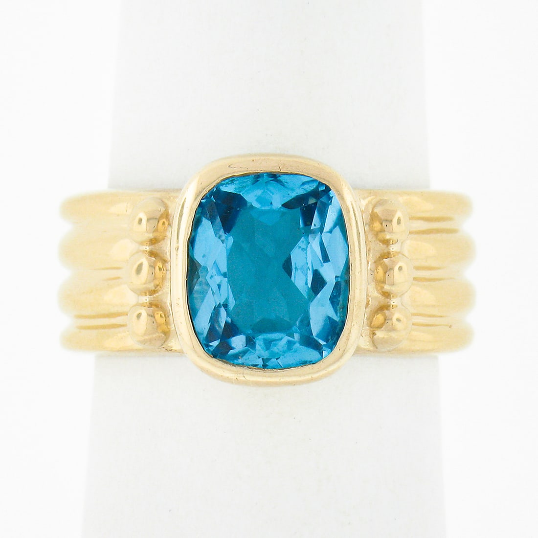 14K Yellow Gold 3.50ct Cushion Blue Topaz Bezel Solitaire Ring: 14K Yellow Gold 3.50ct Cushion Blue Topaz Bezel Solitaire Ring This exquisite solitaire ring is crafted from solid 14K yellow gold and showcases a stunning cushion cut blue topaz, securely bezel set a