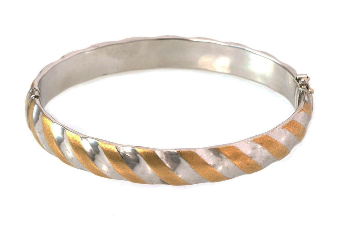 Oval Hinged Bangle Bracelet in 14k Two Tone Gold Made in Italy: Oval Hinged Bangle Bracelet in 14k Two Tone Gold Made in Italy This elegant bangle bracelet is crafted in hollow 14k yellow and white gold, featuring a distinctive slanted stripe pattern that wraps ar