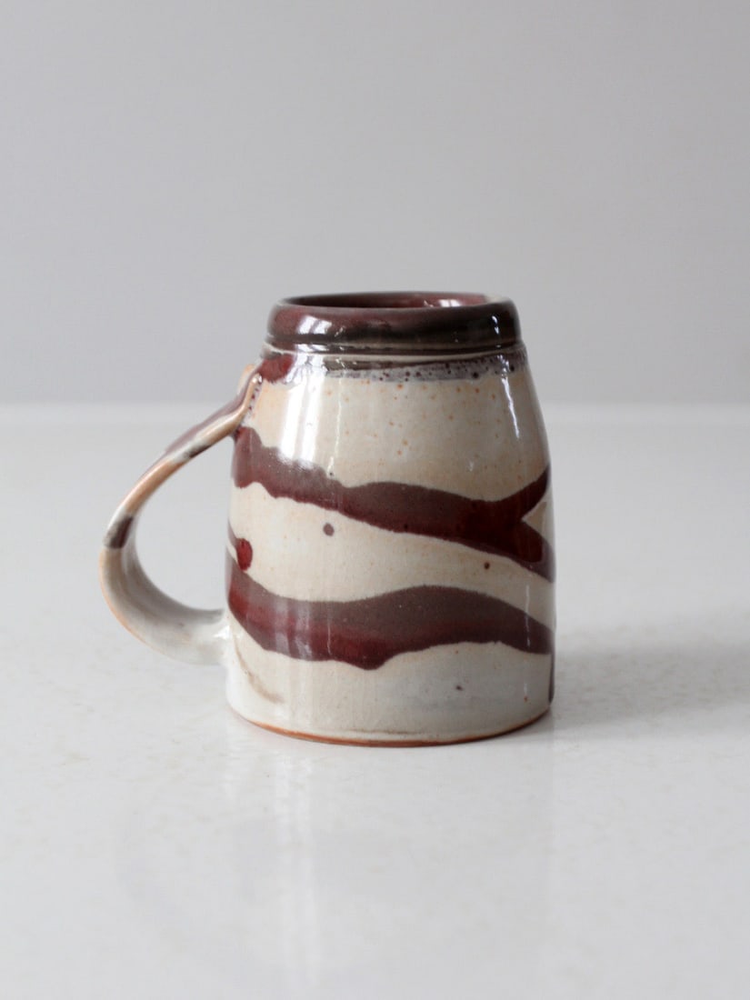 Piper Vintage Studio Pottery Mug with Brown Glaze: Piper Vintage Studio Pottery Mug with Brown Glaze This charming vintage studio pottery mug showcases a gently rounded shape adorned with painterly swirls of deep brown glaze over a warm neutral base.