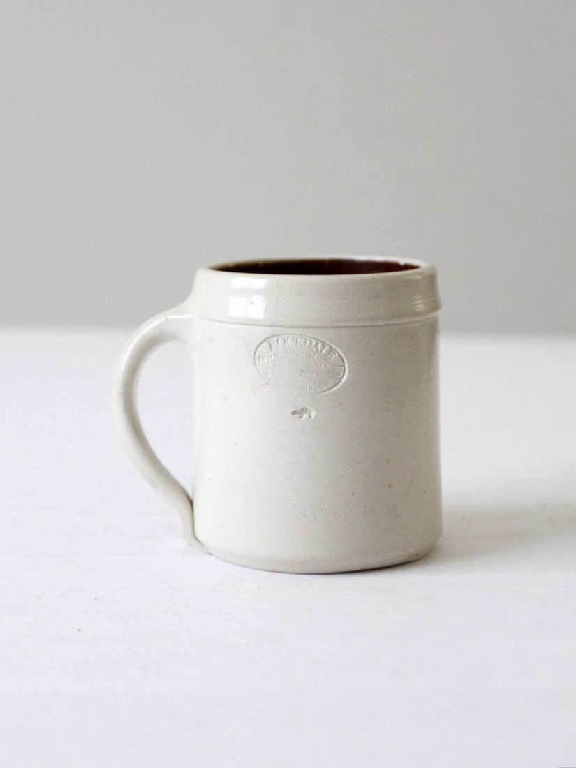 Vintage 1996 Rockdale Union Stoneware Mug with RUS Logo: Vintage 1996 Rockdale Union Stoneware Mug with RUS Logo Discover this vintage Rockdale Union Stoneware mug from 1996, featuring a classic design with a white slip glaze and a rich brown interior. The