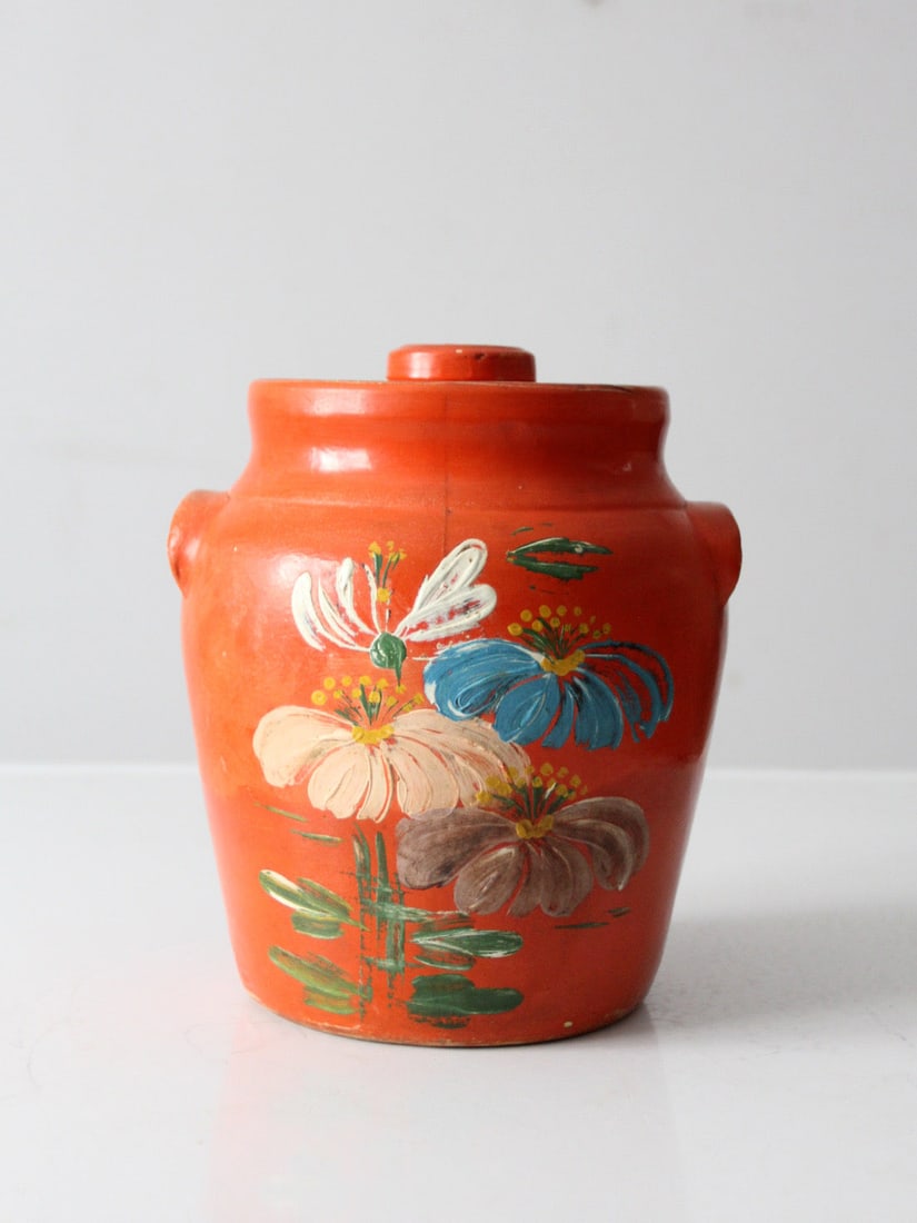 Hand-Painted Folk Art Stoneware Cookie Jar with Floral Design: Hand-Painted Folk Art Stoneware Cookie Jar with Floral Design This antique hand-painted stoneware cookie jar features a vibrant orange finish with a lively floral motif. Its rounded silhouette and for