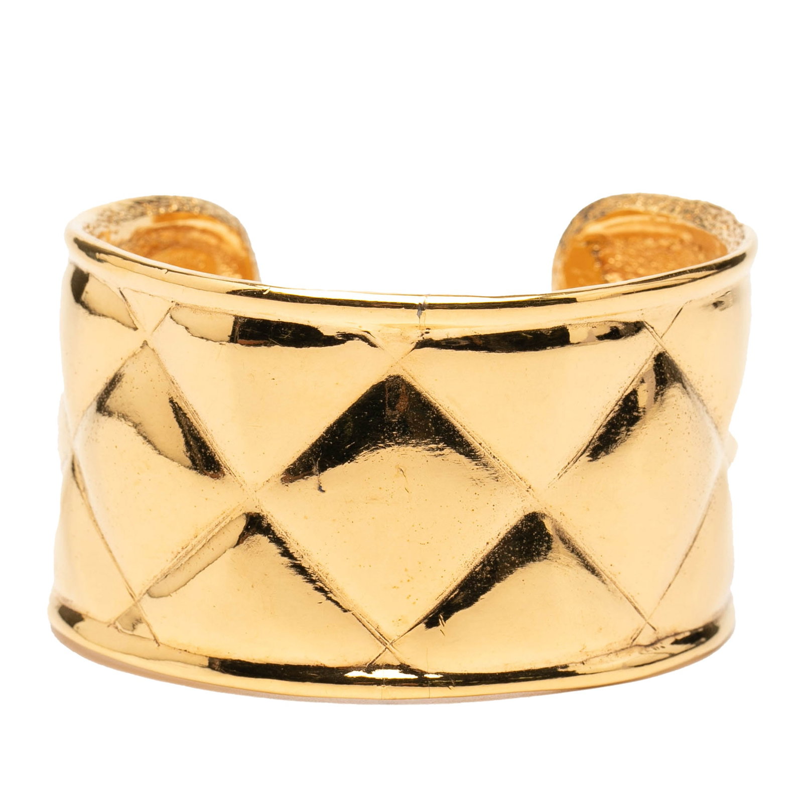 Quilted Gold Plated Cuff Bracelet by Chanel: Quilted Gold Plated Cuff Bracelet by Chanel This Chanel cuff bracelet features a quilted gold-plated metal design. It is a costume piece crafted in France with a gold-tone finish. The bracelet shows s