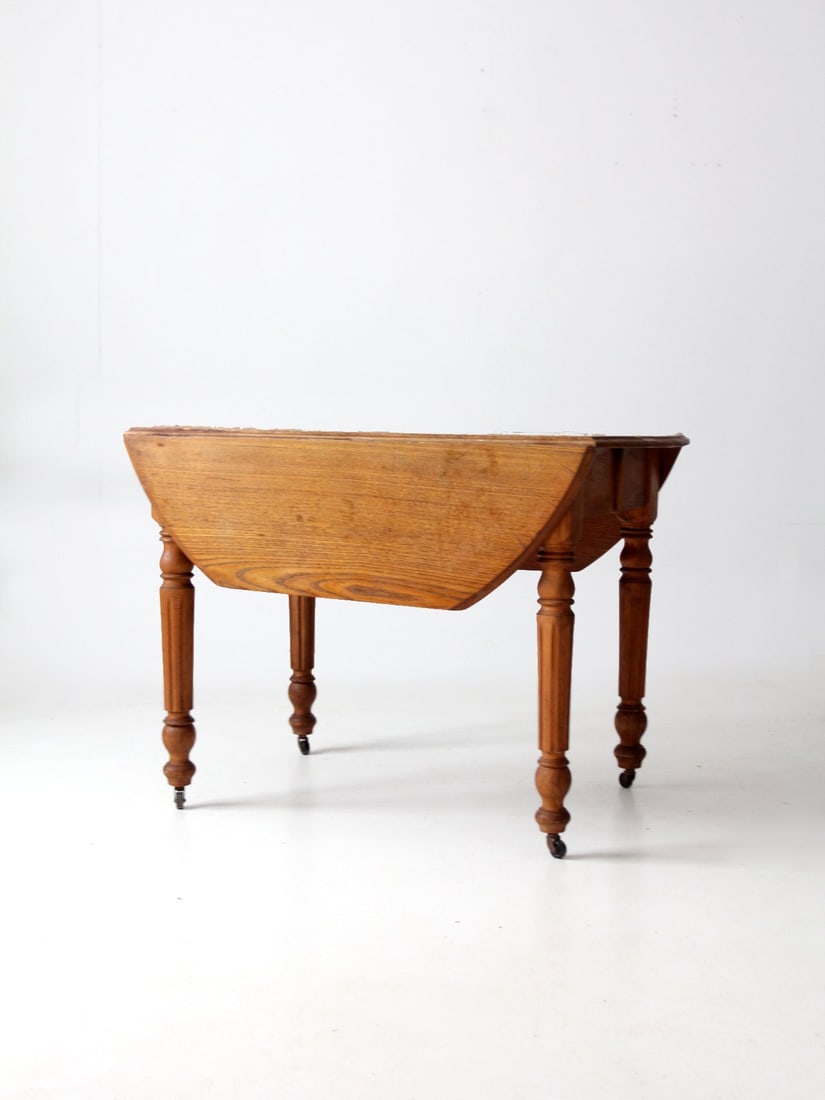 Antique Wooden Drop Leaf Table with Turned Legs and Casters: Antique Wooden Drop Leaf Table with Turned Legs and Casters This antique wooden drop leaf table combines functionality with classic design. Crafted from wood, it features elegant turned legs equipped