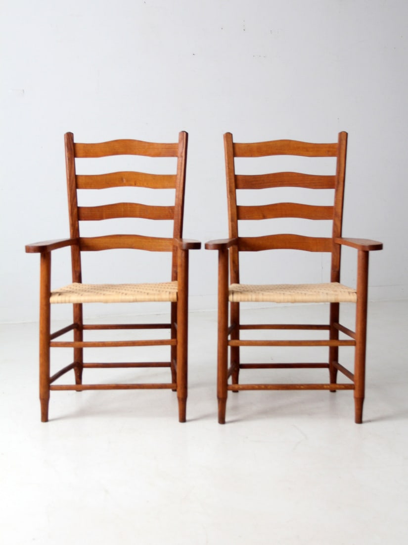 Colonial Style Pair of Vintage Ladder Back Arm Chairs: Colonial Style Pair of Vintage Ladder Back Arm Chairs This pair of vintage arm chairs showcases classic ladder backs and wide arms, embodying the Colonial American design aesthetic. The herringbone wo