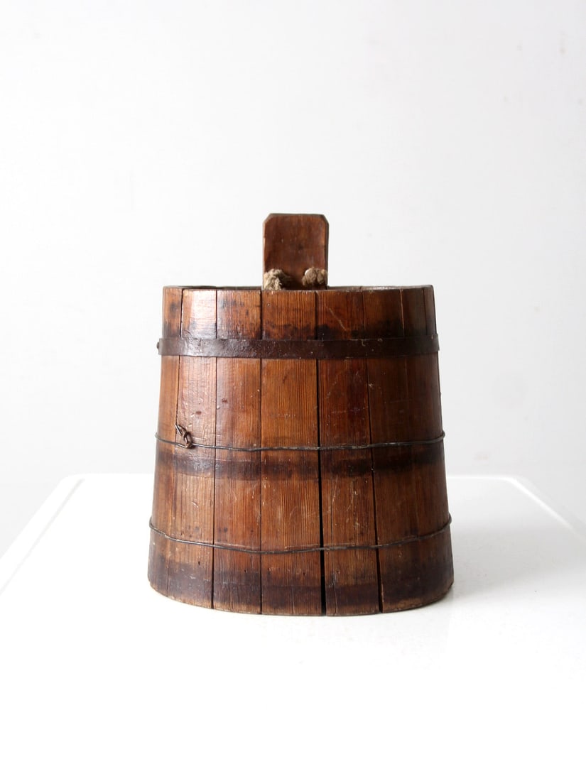 Vintage Handcrafted Wood Stave Cask with Rope Handle: Vintage Handcrafted Wood Stave Cask with Rope Handle This antique wood stave cask pail is a handcrafted treasure, featuring a tapered stave construction complemented by wire and iron banding. Original
