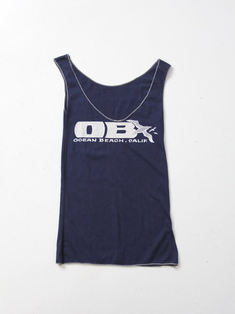 Vintage Navy Blue Ocean Beach Tank Top with Beach Graphic: Vintage Navy Blue Ocean Beach Tank Top with Beach Graphic This vintage Ocean Beach, California tank top features a classic navy blue color with a stylish v-neck collar and contrasting white stitching.