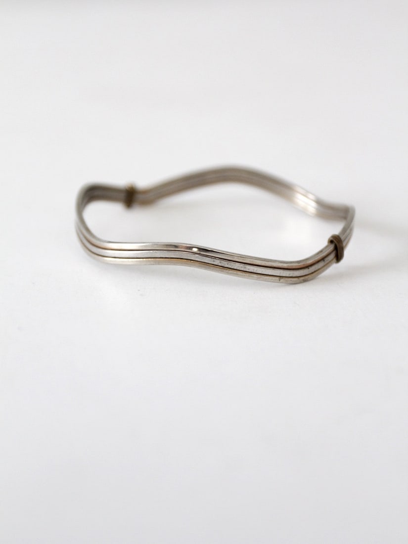 1980s Vintage Silver Tone Wavy Bangle Bracelet: 1980s Vintage Silver Tone Wavy Bangle Bracelet This vintage wavy bangle bracelet from the 1980s features a slender design with a unique wavy pattern complemented by slender bands on the sides. The bra