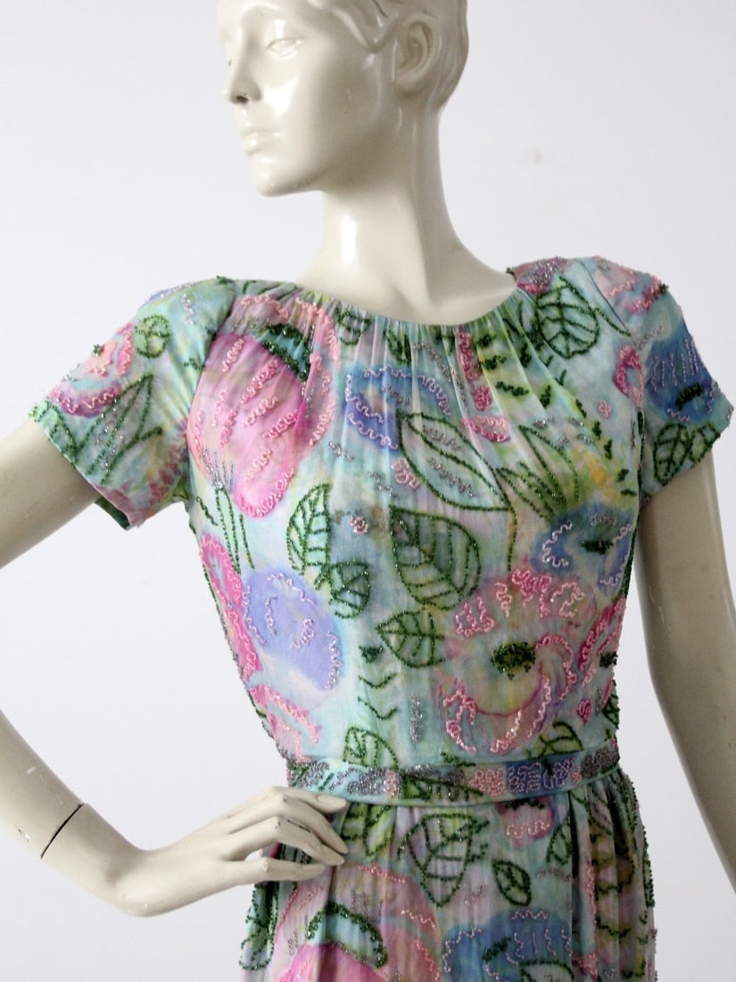1960s Vintage Beaded Chiffon Dress Watercolor Floral Print: 1960s Vintage Beaded Chiffon Dress Watercolor Floral Print This exquisite vintage 1960s dress showcases a stunning beaded watercolor print. Crafted with delicate layers of chiffon, the fitted silhouet