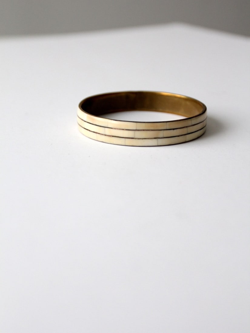 Vintage 70s Brass Bangle Bracelet with Bone Inlay Design: Vintage 70s Brass Bangle Bracelet with Bone Inlay Design This vintage 70s bangle bracelet is a stunning piece that showcases a unique bone inlay design set in a brass slip-on construction. The bracele