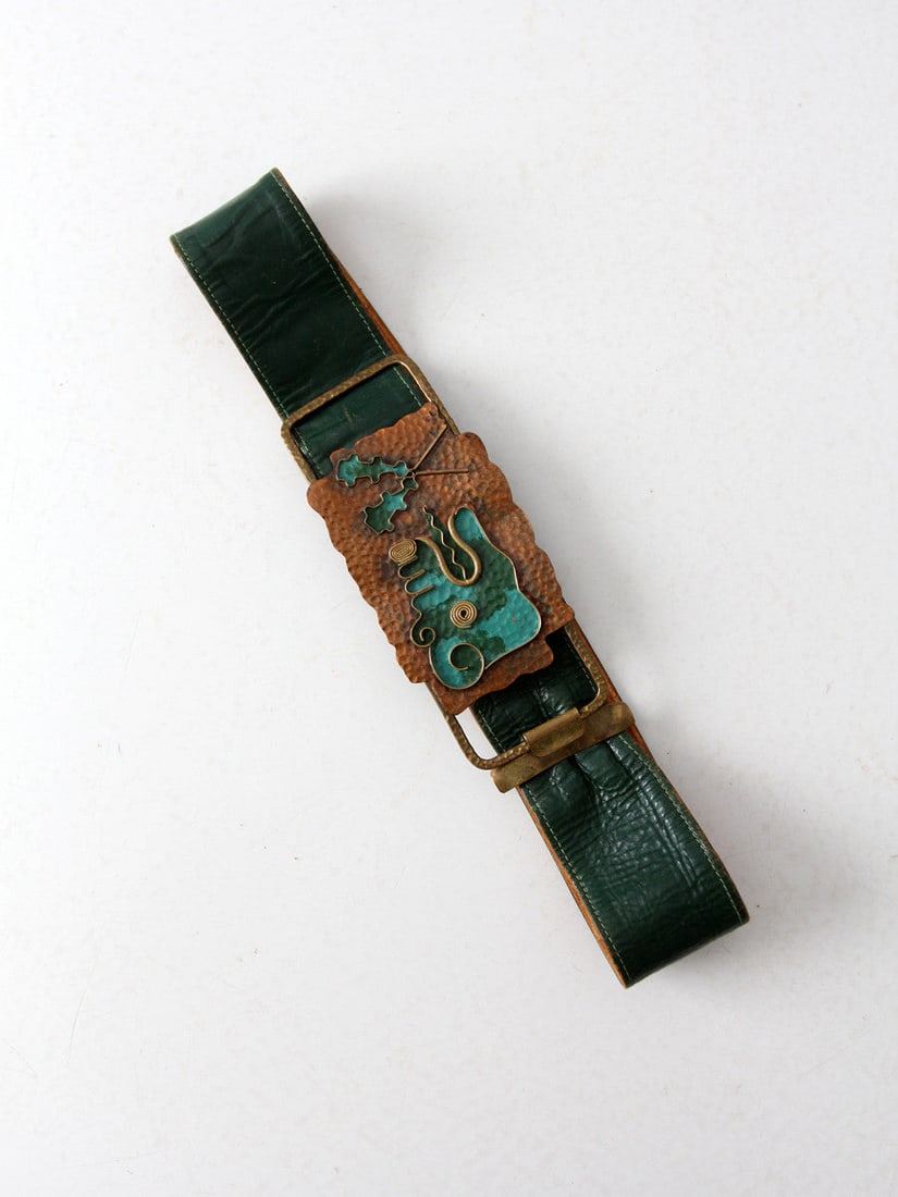 Vintage 80s Green Leather Belt with Abstract Brass Buckle: Vintage 80s Green Leather Belt with Abstract Brass Buckle This vintage 1980s green leather belt features a striking large abstract art buckle, adding a unique flair to any outfit. The soft leather str