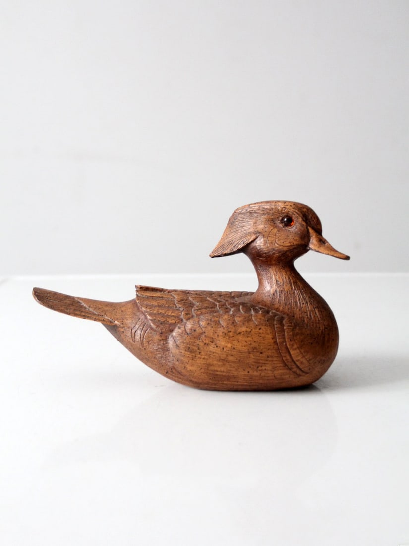 Carved Midcentury Wooden Duck Sculpture with Glass Eyes: Carved Midcentury Wooden Duck Sculpture with Glass Eyes This mid-century carved wood duck figurine features gentle contours and subtle feather detailing. The piece is finished in warm wood tones that 