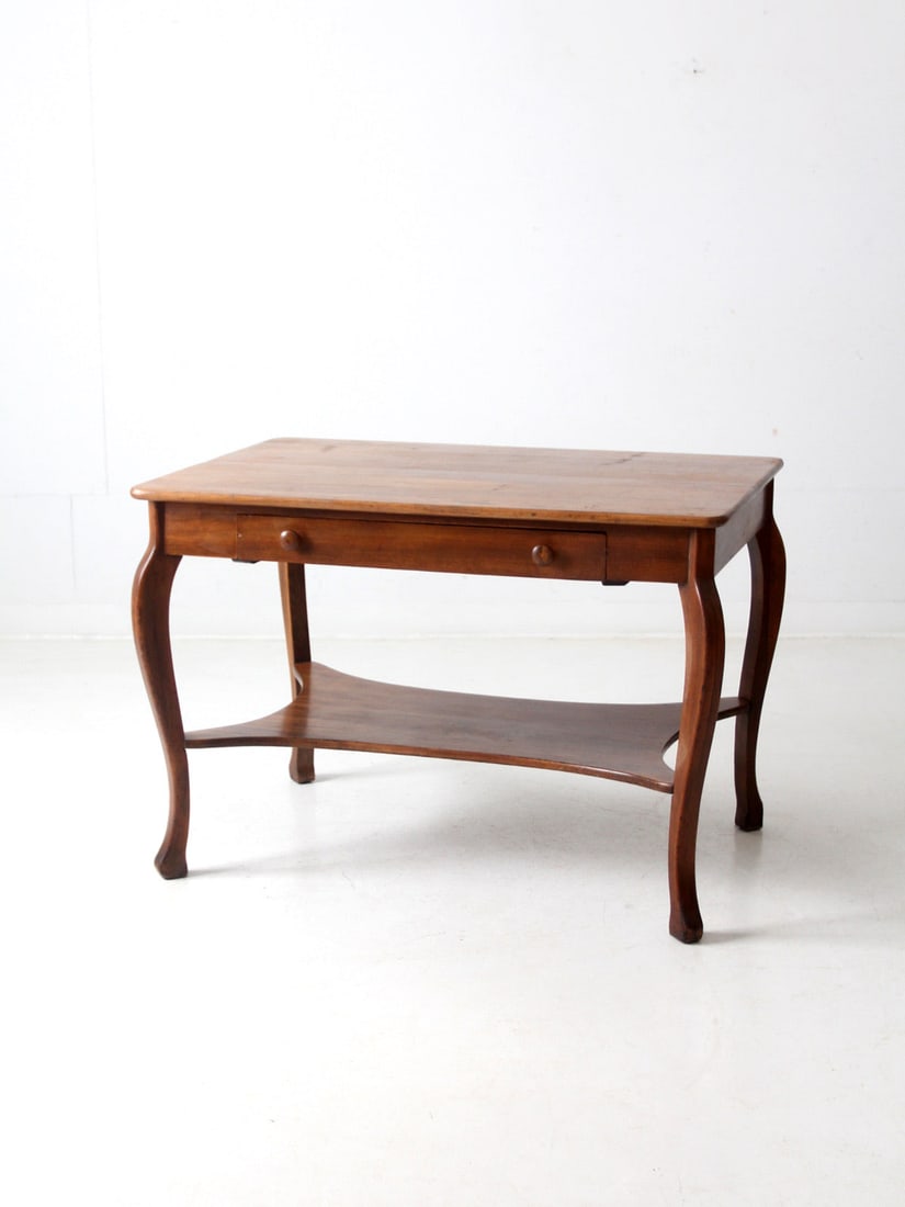 French Provincial Antique Library Table with Drawer and Stretcher Shelf: French Provincial Antique Library Table with Drawer and Stretcher Shelf This antique library table features a timeless French Provincial design, characterized by its elegant cabriole legs and bun feet